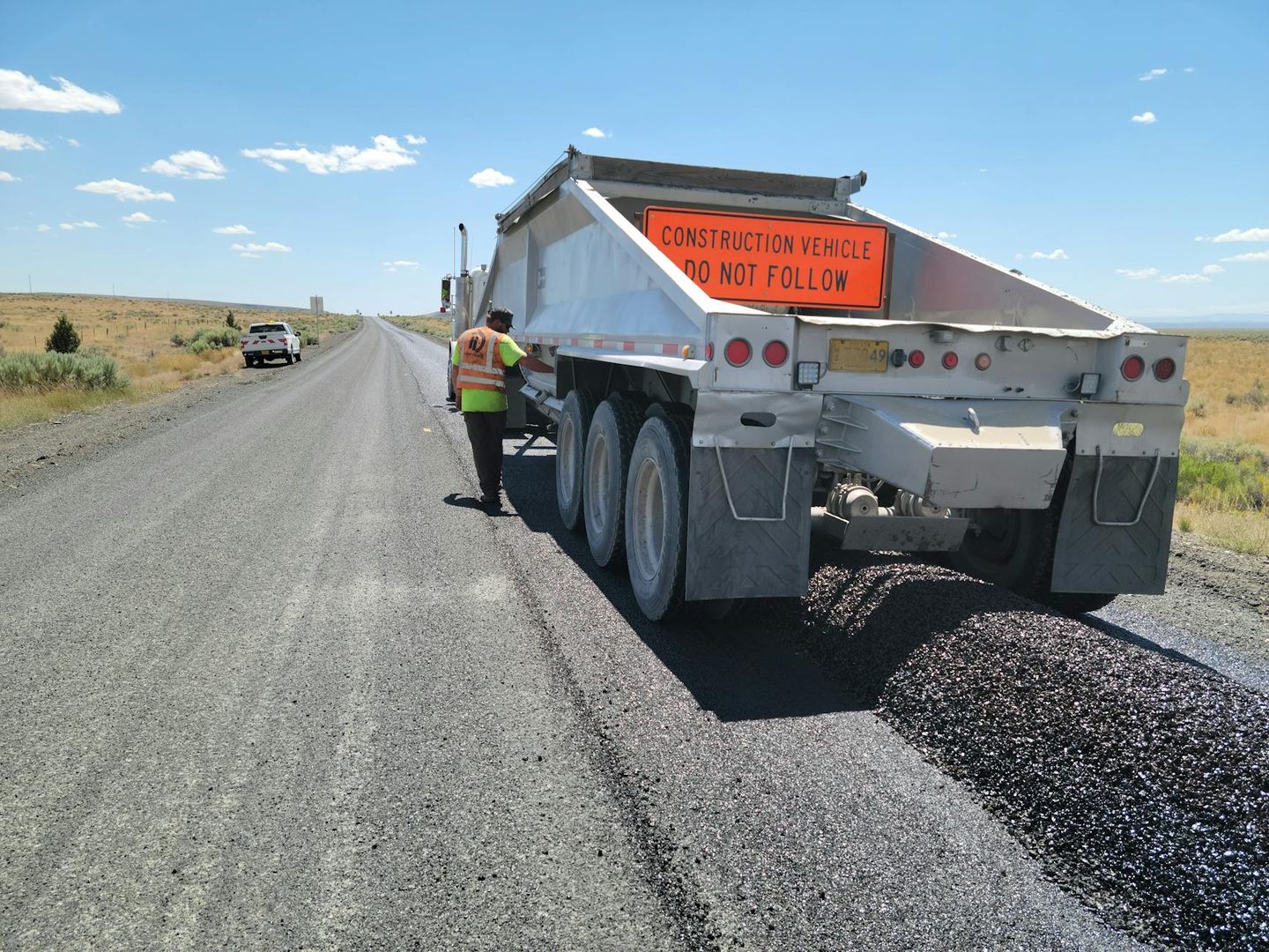 Baustellenfahrzeug verteilt frischen Asphalt auf einer Landstraße.